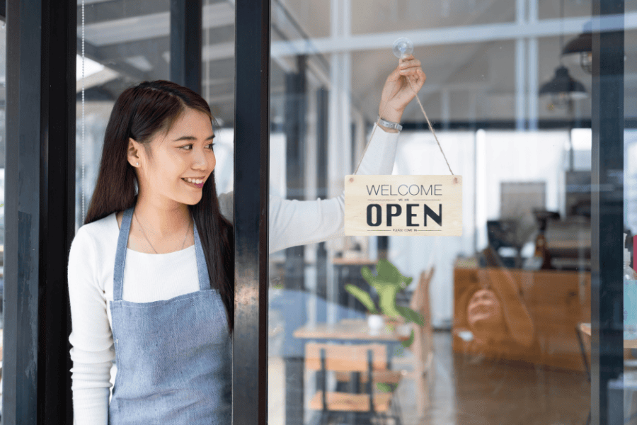 A woman small business owner wearing an apron with an open sign