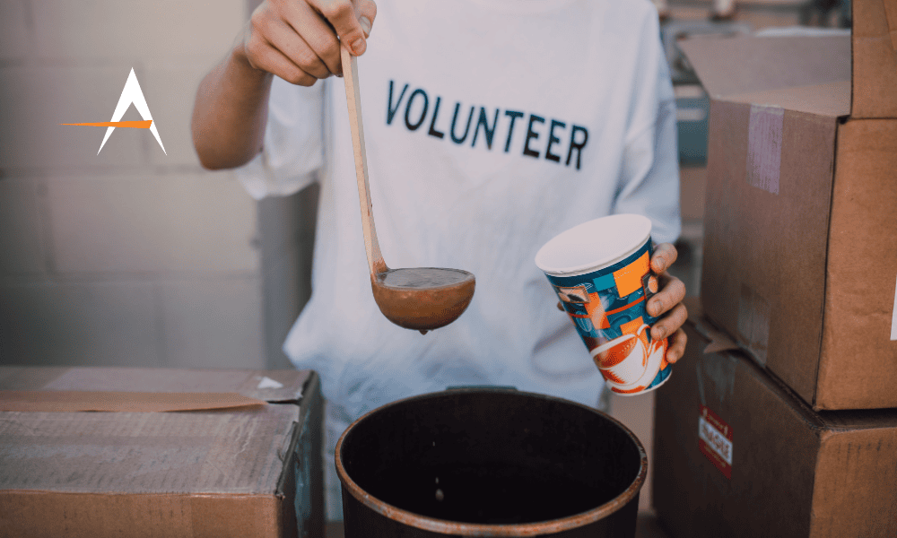An image of a person wearing a 'volunteer' shirt serving soup outdoors
